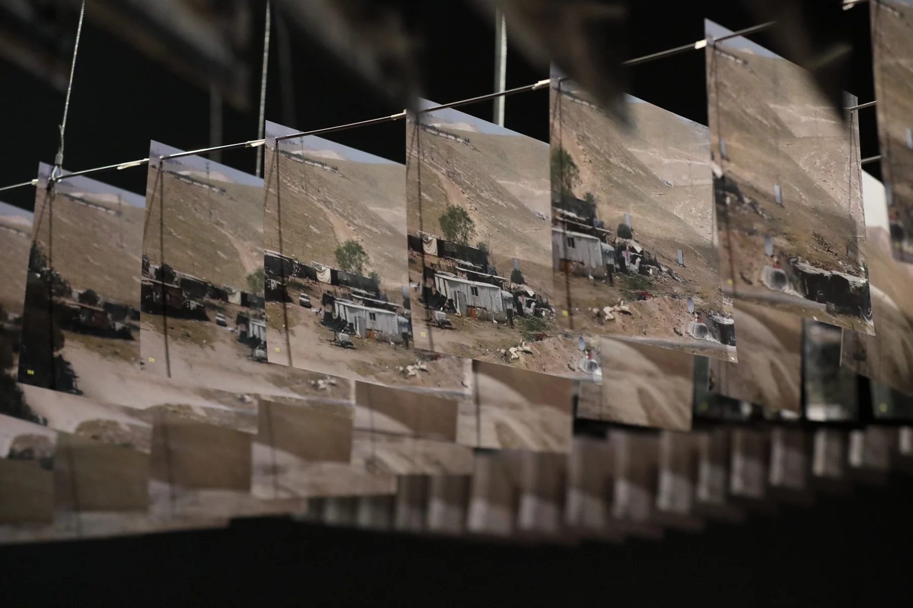 A sequence of suspended printed landscape fragments in a dark gallery.